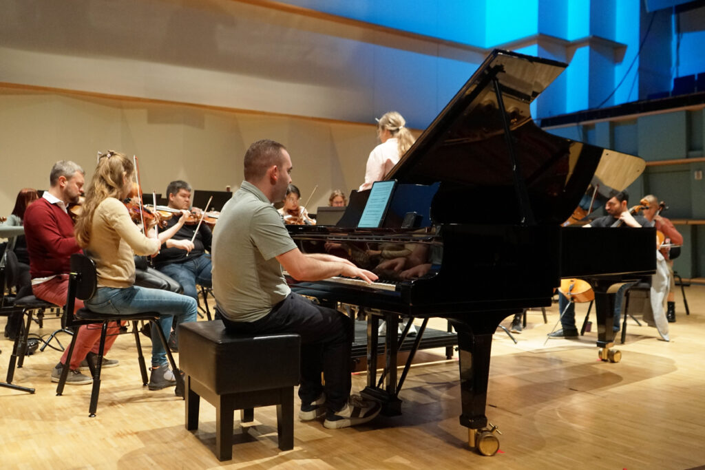 Mackenzie Melemed soittaa pianoa Promenadisalissa orkesteri taustalla.